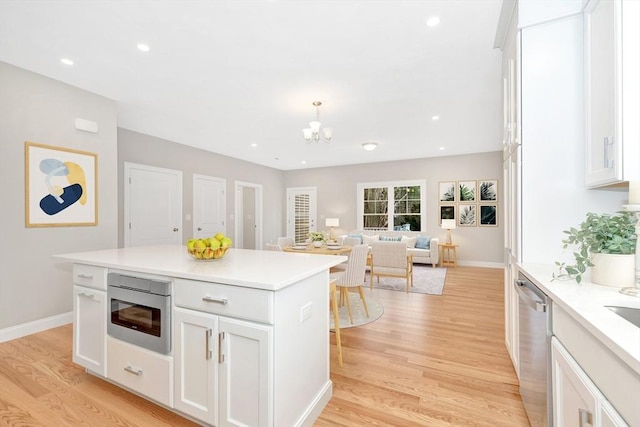 kitchen with light wood finished floors, white cabinets, stainless steel dishwasher, and light countertops