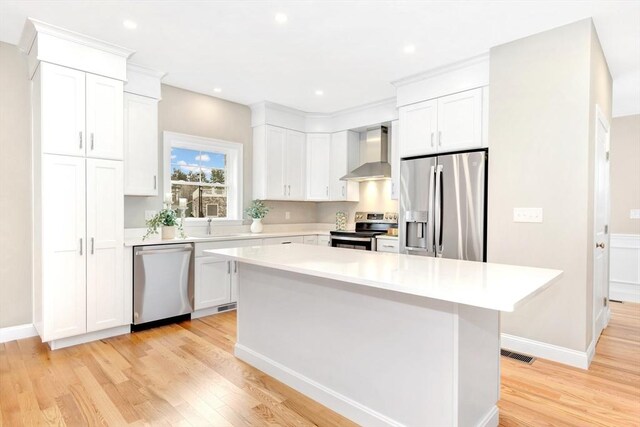 kitchen featuring light wood finished floors, stainless steel appliances, light countertops, white cabinets, and wall chimney range hood