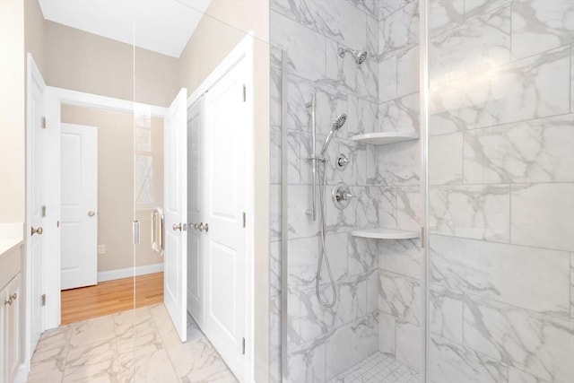 full bath featuring marble finish floor, a marble finish shower, baseboards, and vanity