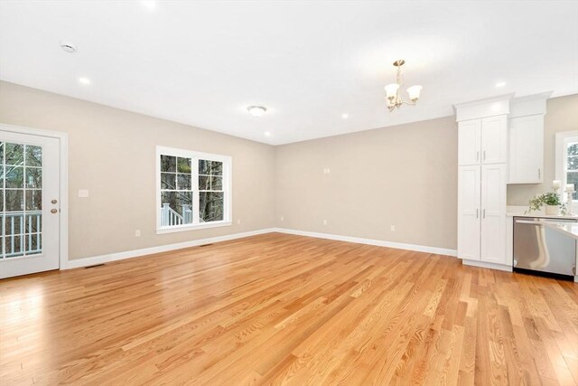 unfurnished living room featuring a chandelier, light wood-type flooring, a healthy amount of sunlight, and baseboards