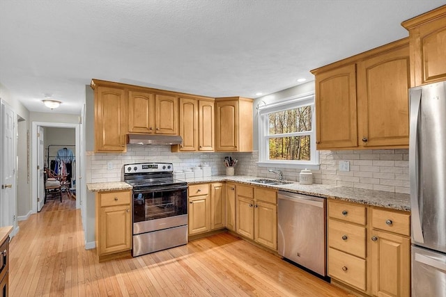 kitchen with sink, light stone counters, light hardwood / wood-style flooring, appliances with stainless steel finishes, and decorative backsplash