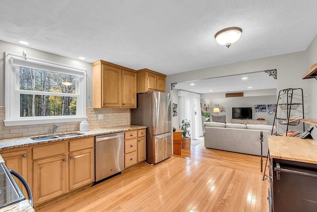 kitchen featuring sink, appliances with stainless steel finishes, tasteful backsplash, light stone counters, and light hardwood / wood-style floors