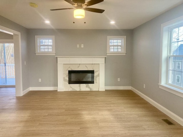 unfurnished living room featuring visible vents, light wood finished floors, ceiling fan, and a premium fireplace