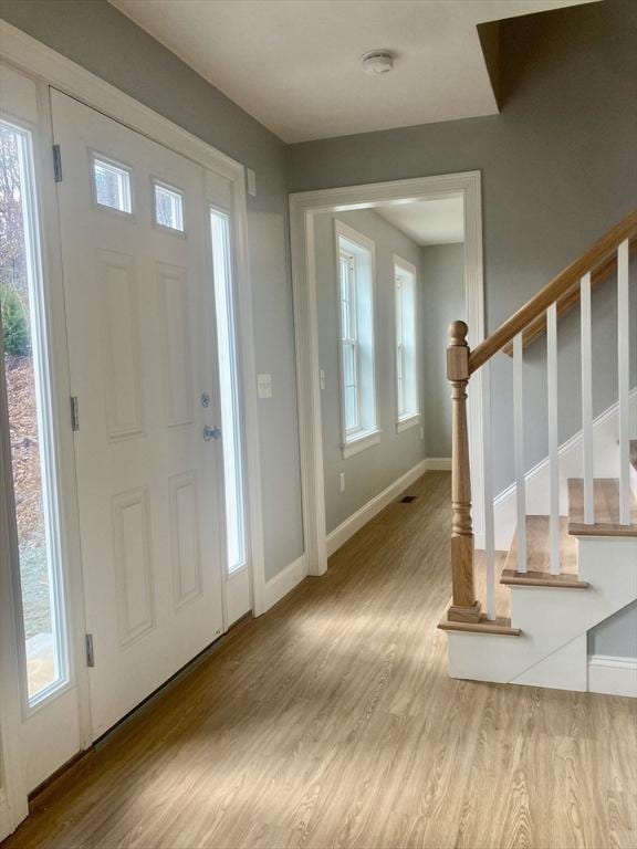 entrance foyer with stairs, baseboards, a healthy amount of sunlight, and wood finished floors