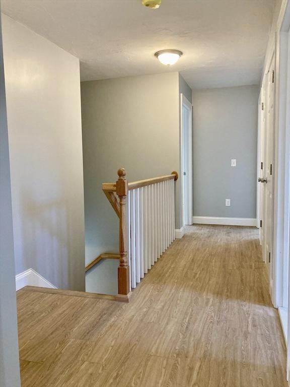hall with baseboards, wood finished floors, and an upstairs landing