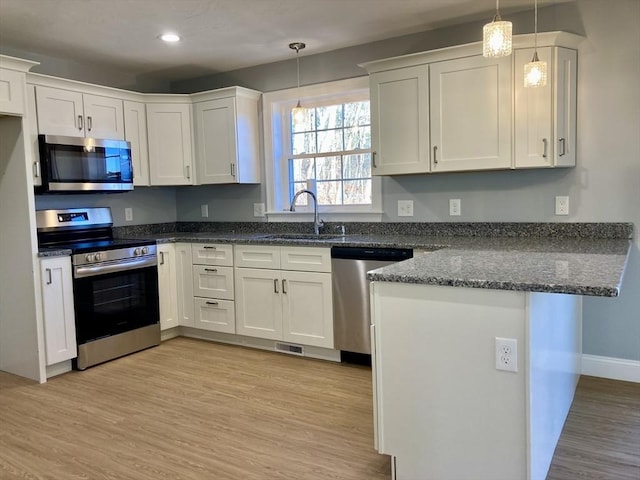 kitchen featuring a peninsula, white cabinetry, a sink, light wood-style flooring, and stainless steel appliances