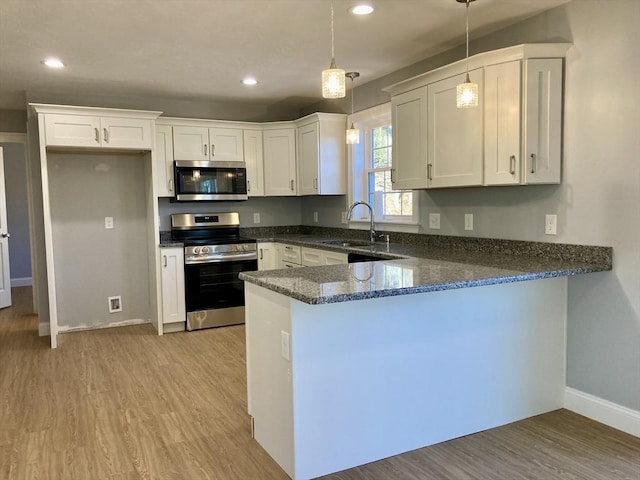 kitchen with a peninsula, dark stone counters, white cabinets, a sink, and stainless steel appliances