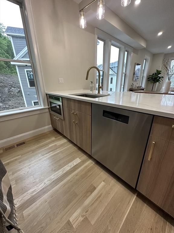 kitchen featuring stainless steel dishwasher, pendant lighting, light wood-type flooring, and sink