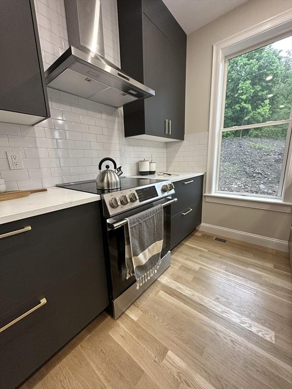 kitchen with stainless steel range, decorative backsplash, light hardwood / wood-style floors, and wall chimney range hood