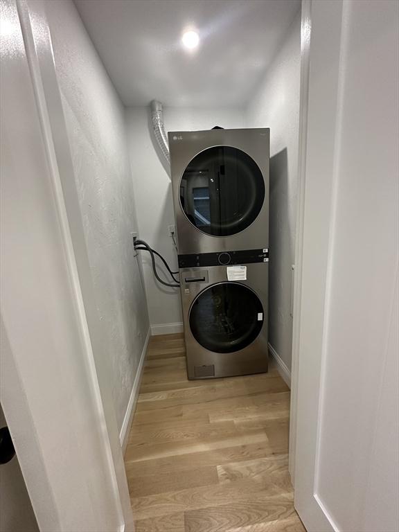 washroom with stacked washing maching and dryer and light hardwood / wood-style floors