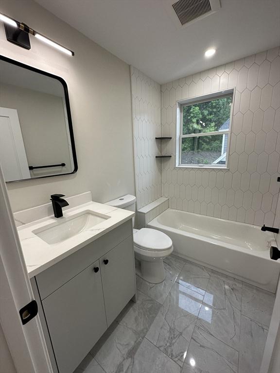 full bathroom with tiled shower / bath, vanity, and toilet