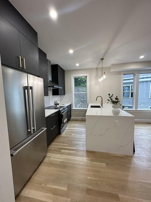 kitchen featuring sink, stainless steel appliances, an island with sink, light hardwood / wood-style floors, and decorative light fixtures