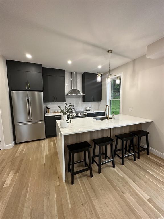 kitchen with wall chimney range hood, pendant lighting, a breakfast bar area, appliances with stainless steel finishes, and light wood-type flooring