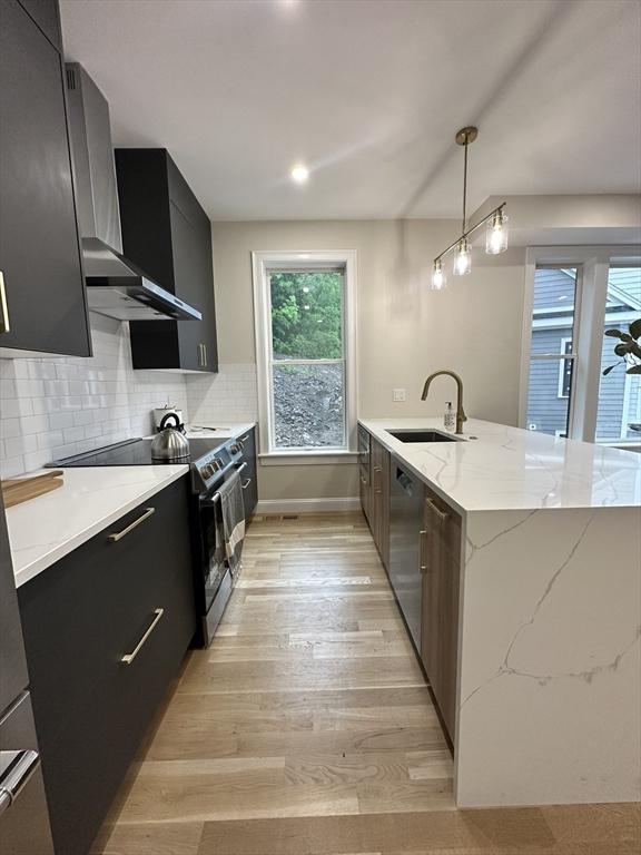 kitchen featuring light stone counters, stainless steel appliances, sink, light hardwood / wood-style flooring, and hanging light fixtures