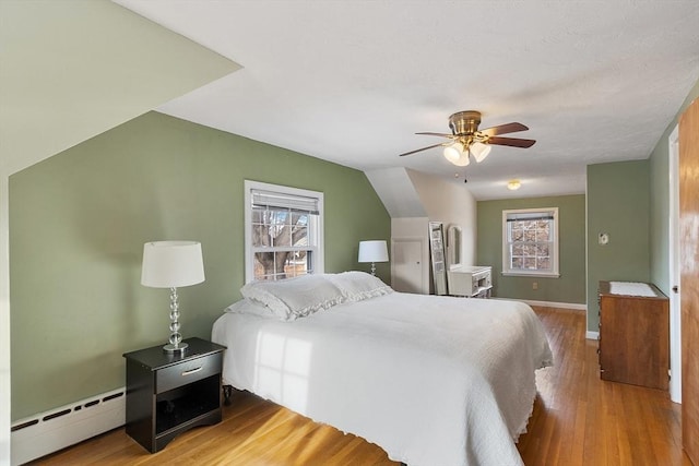 bedroom featuring hardwood / wood-style flooring, vaulted ceiling, a baseboard heating unit, and ceiling fan