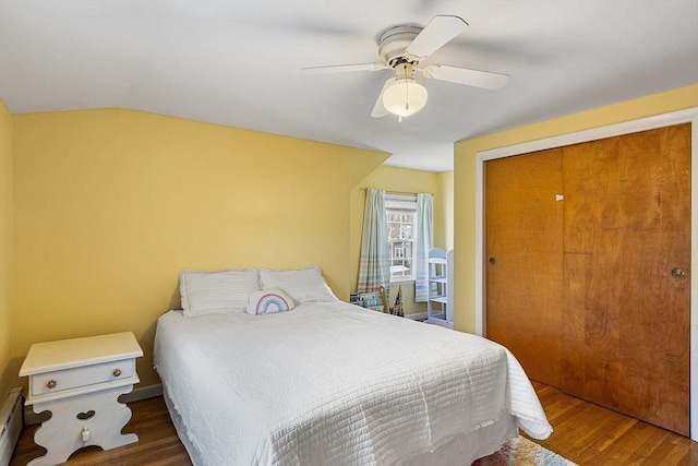 bedroom featuring ceiling fan, baseboard heating, hardwood / wood-style floors, vaulted ceiling, and a closet