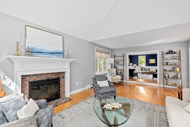 living room with lofted ceiling, light hardwood / wood-style floors, and a brick fireplace