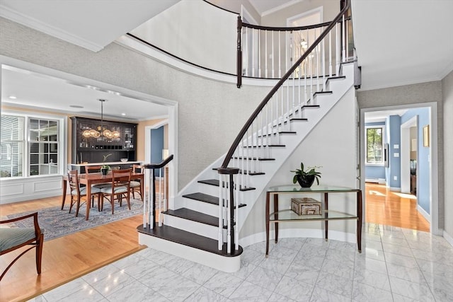 stairs featuring a towering ceiling, ornamental molding, and a notable chandelier