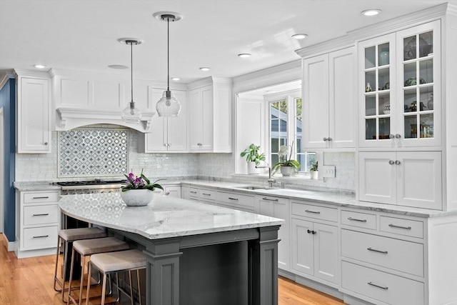 kitchen with a center island, custom range hood, white cabinets, decorative light fixtures, and light wood-type flooring