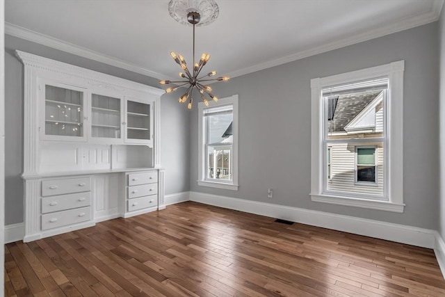 unfurnished dining area featuring dark wood-type flooring, visible vents, baseboards, ornamental molding, and an inviting chandelier