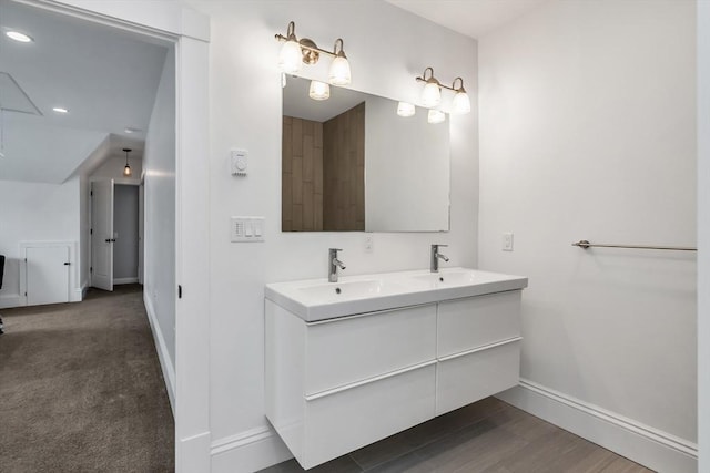 bathroom with wood finished floors, a sink, baseboards, and double vanity