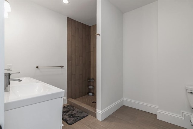 bathroom with recessed lighting, toilet, a tile shower, wood finished floors, and baseboards