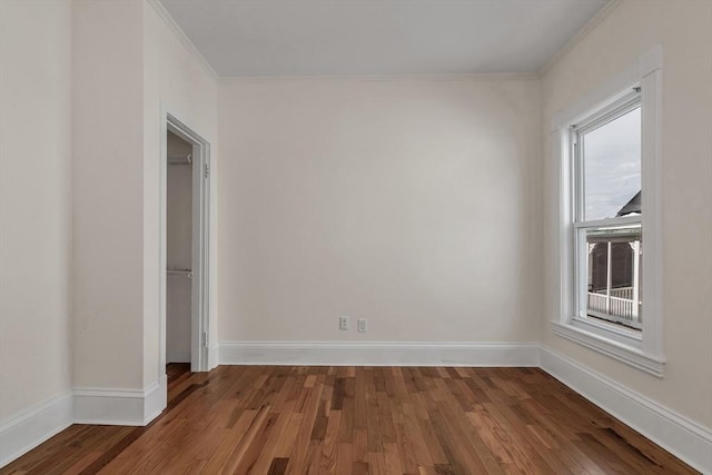 empty room featuring crown molding, wood finished floors, and baseboards