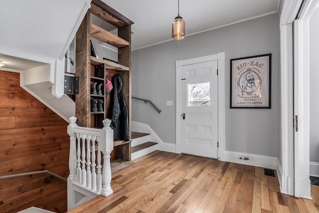 entryway with light wood-type flooring, baseboards, stairway, and ornamental molding