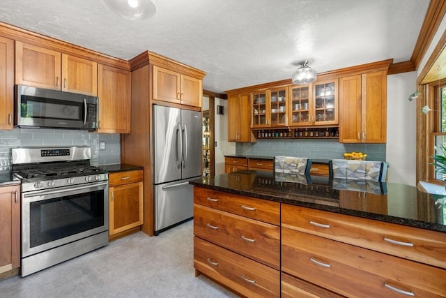 198 Edge Hill Rd, Sharon, MA 02067 - kitchen with appliances with stainless steel finishes, brown cabinetry, backsplash, glass insert cabinets, and a textured ceiling