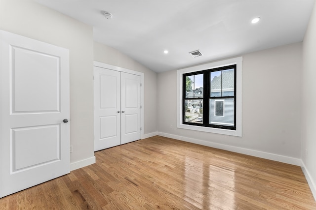 unfurnished bedroom with light wood-type flooring, a closet, and lofted ceiling