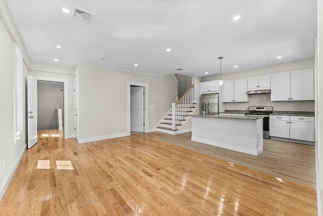 kitchen featuring light wood-type flooring, appliances with stainless steel finishes, white cabinetry, and an island with sink