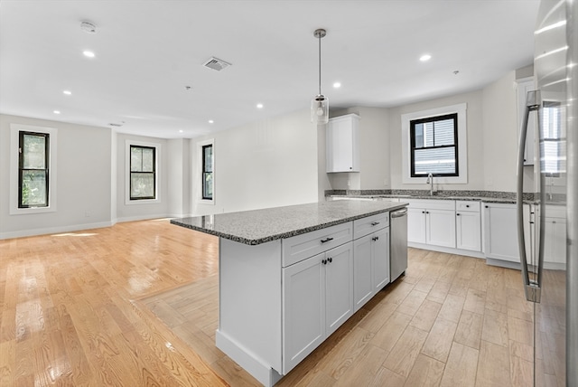 kitchen featuring white cabinets, light wood-type flooring, appliances with stainless steel finishes, stone countertops, and a kitchen island