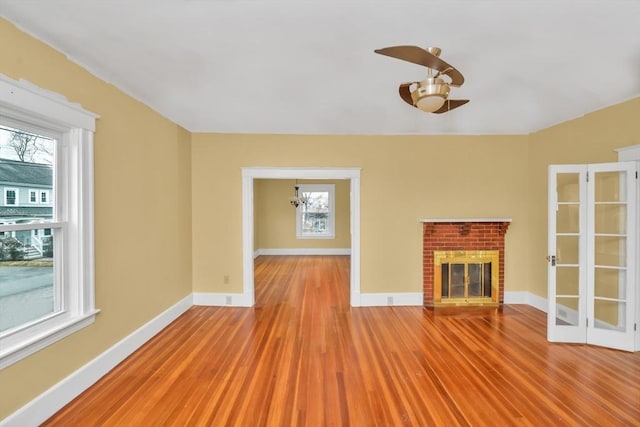 unfurnished living room featuring a brick fireplace, baseboards, and wood finished floors