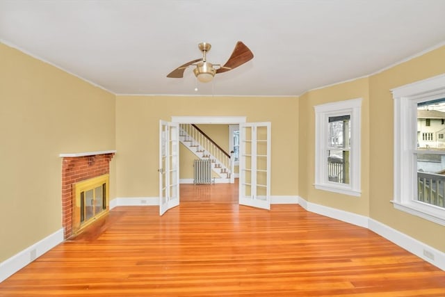 unfurnished living room featuring french doors, a ceiling fan, a brick fireplace, light wood-type flooring, and baseboards