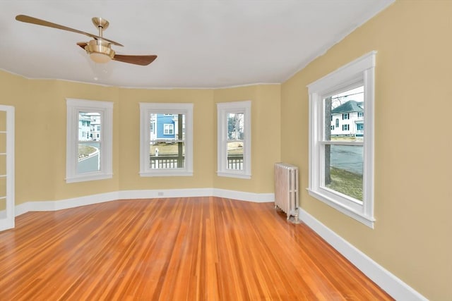 empty room with light wood-type flooring, radiator heating unit, baseboards, and a ceiling fan