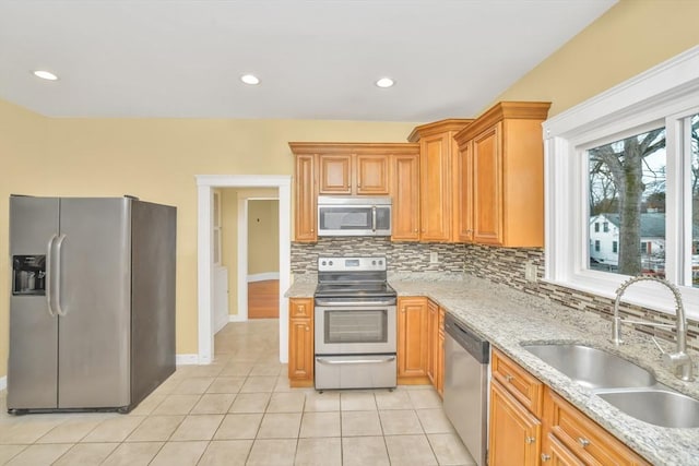 kitchen featuring light tile patterned floors, stainless steel appliances, a sink, decorative backsplash, and light stone countertops