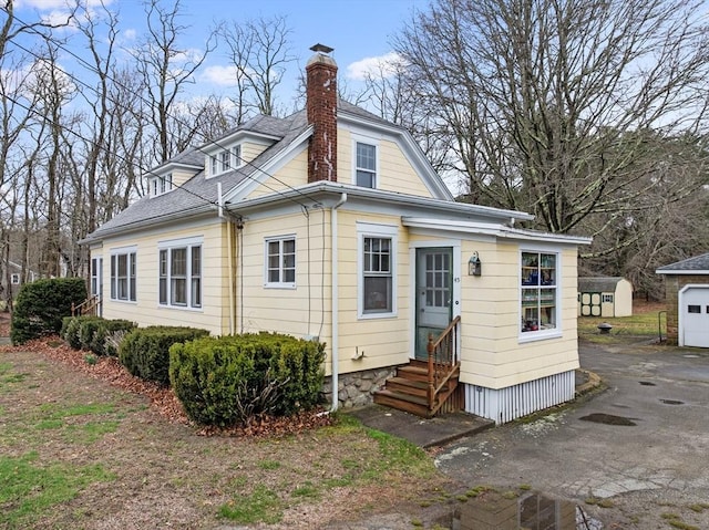 rear view of property with entry steps, a chimney, and aphalt driveway