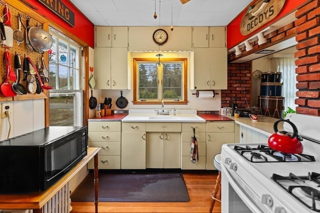 kitchen featuring white gas range oven, black microwave, wood finished floors, light countertops, and a sink