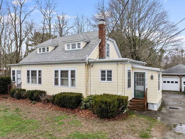 view of front of property featuring entry steps, a detached garage, a chimney, an outdoor structure, and roof with shingles