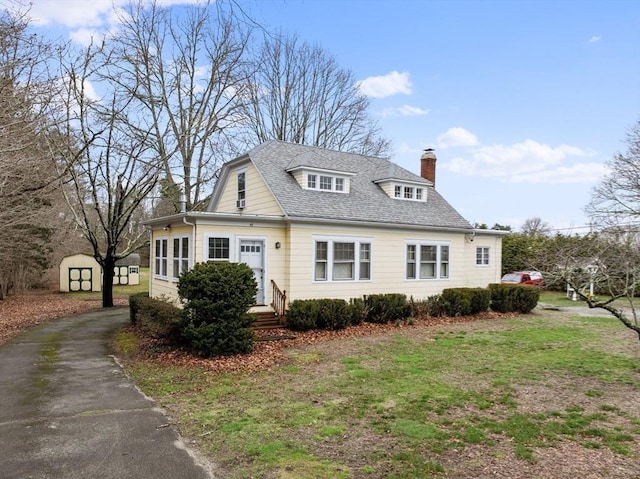 view of front of house featuring an outbuilding, aphalt driveway, entry steps, a storage unit, and a chimney