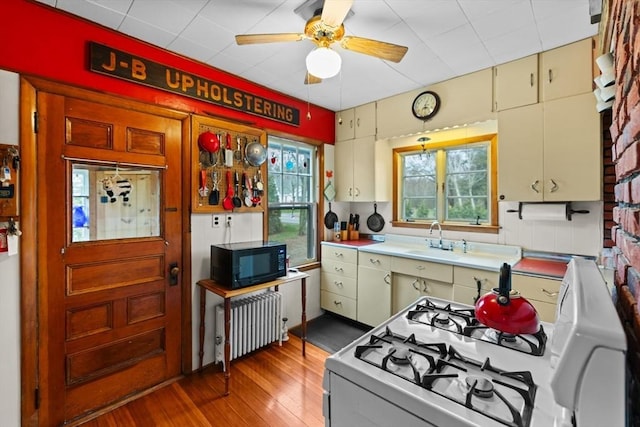 kitchen featuring ceiling fan, white gas stove, black microwave, wood finished floors, and radiator heating unit