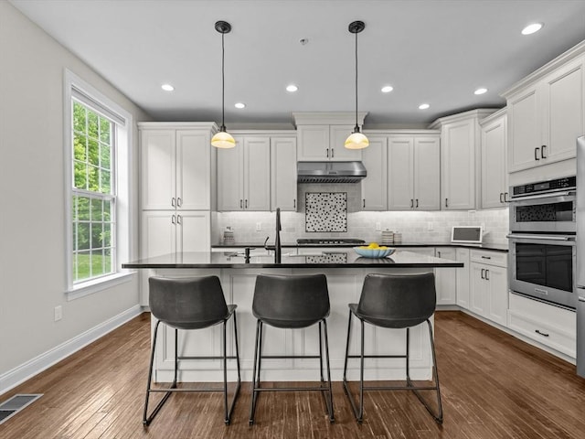 79 Townsend Blvd Unit 79, Westborough, MA 01581 - kitchen with double oven, dark countertops, under cabinet range hood, backsplash, and a breakfast bar area