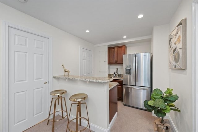 kitchen with a kitchen bar, light stone counters, stainless steel fridge with ice dispenser, light carpet, and kitchen peninsula