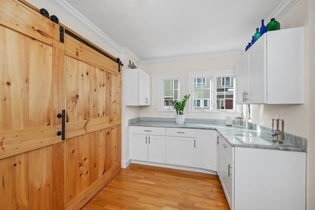 kitchen with crown molding, a barn door, white cabinets, and light hardwood / wood-style floors