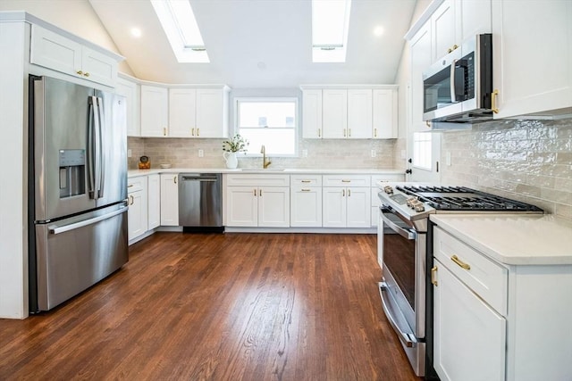 kitchen featuring lofted ceiling with skylight, appliances with stainless steel finishes, white cabinets, and sink