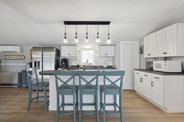 kitchen featuring dark countertops, a sink, stainless steel fridge with ice dispenser, white microwave, and an AC wall unit