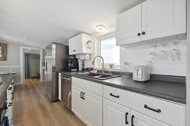 kitchen with stainless steel dishwasher, a sink, wood finished floors, and dark countertops