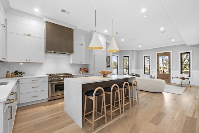 kitchen with light hardwood / wood-style flooring, wall chimney range hood, stainless steel range, a kitchen island, and white cabinetry