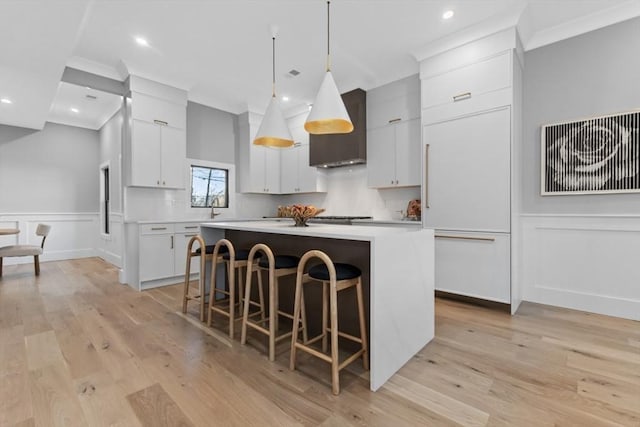 kitchen featuring custom exhaust hood, a center island, a kitchen bar, white cabinets, and decorative light fixtures