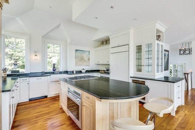 31 Moss Rd, Yarmouth, MA 02673 - kitchen with dark countertops, a center island, glass insert cabinets, light wood finished floors, and appliances with stainless steel finishes